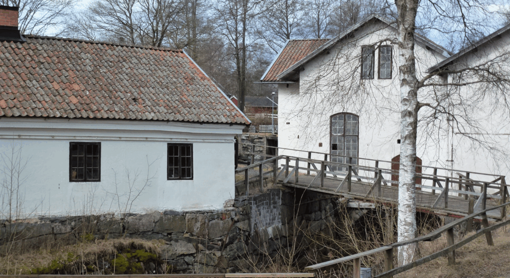 Äldre vitkalkade byggnader där även en bro över ett vattendrag skymtas.