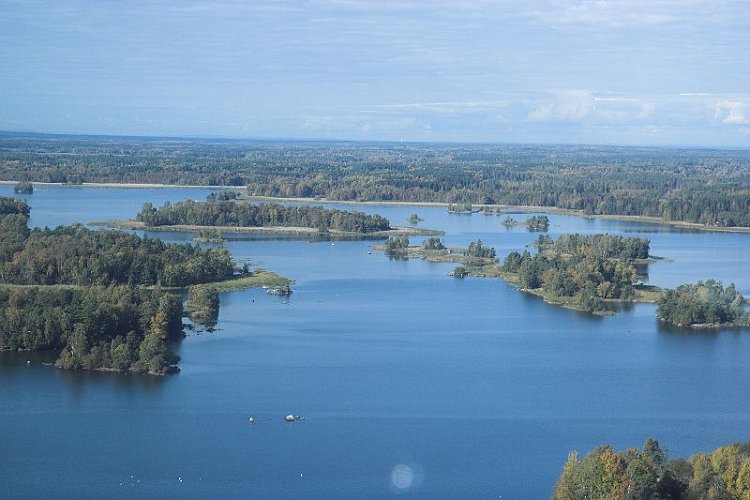 Flygfoto över sjö med skog i bakgrunden och skogsklädda öar i vattnet