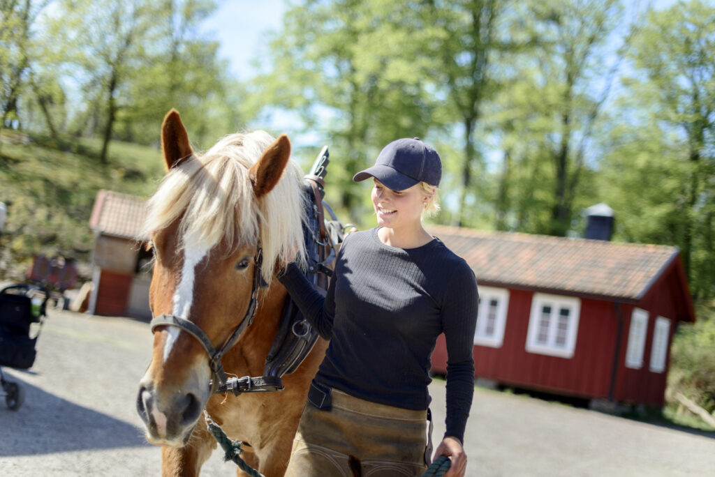 En ung kvinna med keps tar hand om en häst