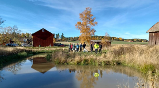 Flera personer står samlade runt ett vattendrag.