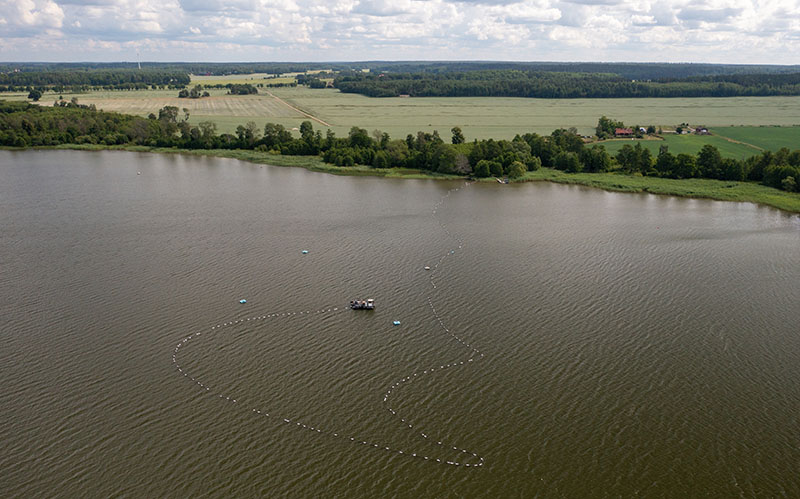 En vy ovanifrån över en sjö och ett jordbrukslandskap. I sjön syns en flotte.